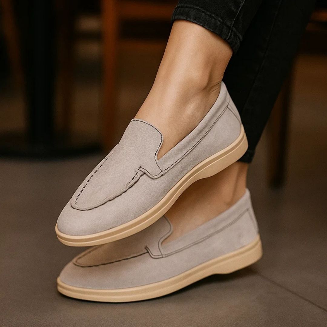 Gray loafers with beige soles worn by a person on a blurred background