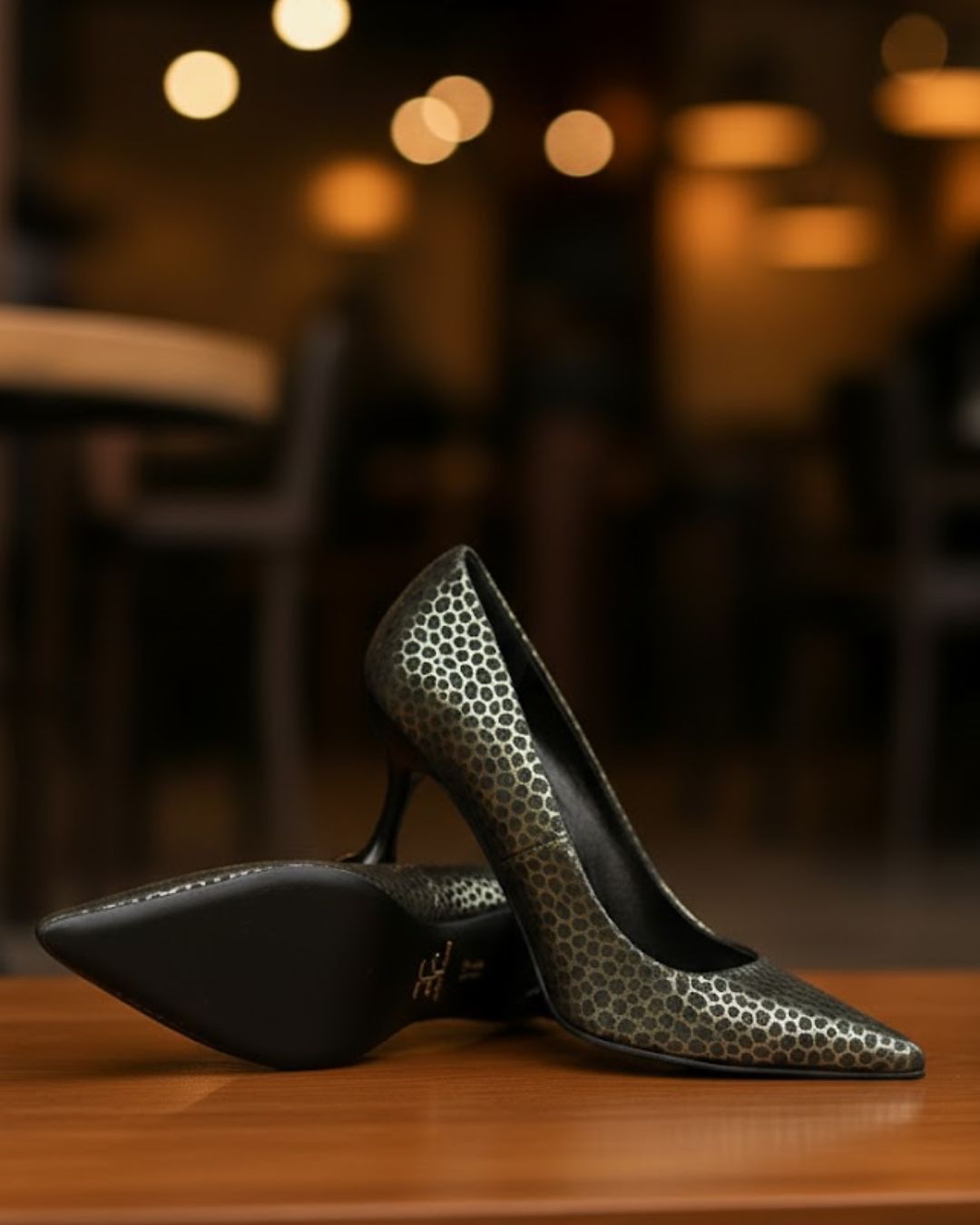 Pair of black high-heeled shoes with silver pattern on a wooden surface, blurred restaurant background