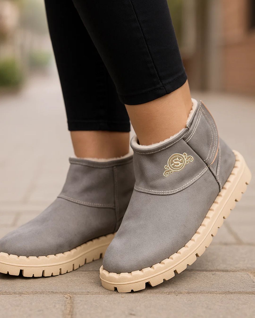 Gray ankle boots with beige soles worn by a person on a stone pavement.