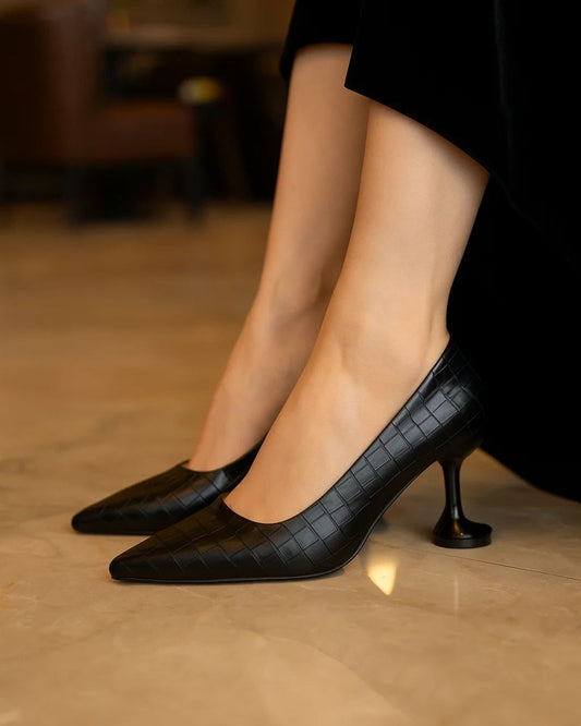 Black high-heeled shoes worn by a person on a blurred indoor background
