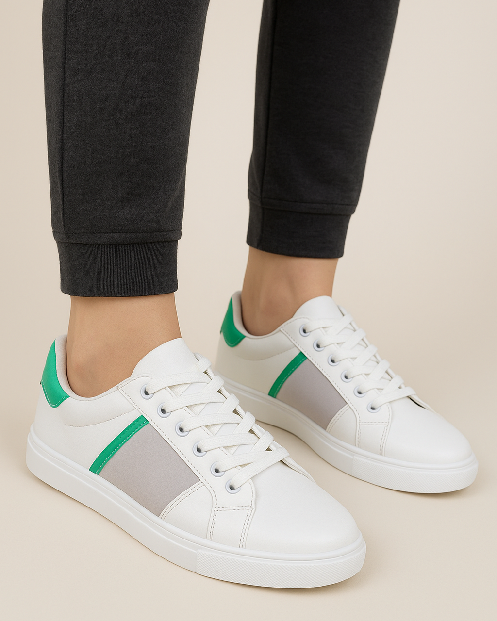 White sneakers with green and gray accents worn by a person in black pants on a beige background