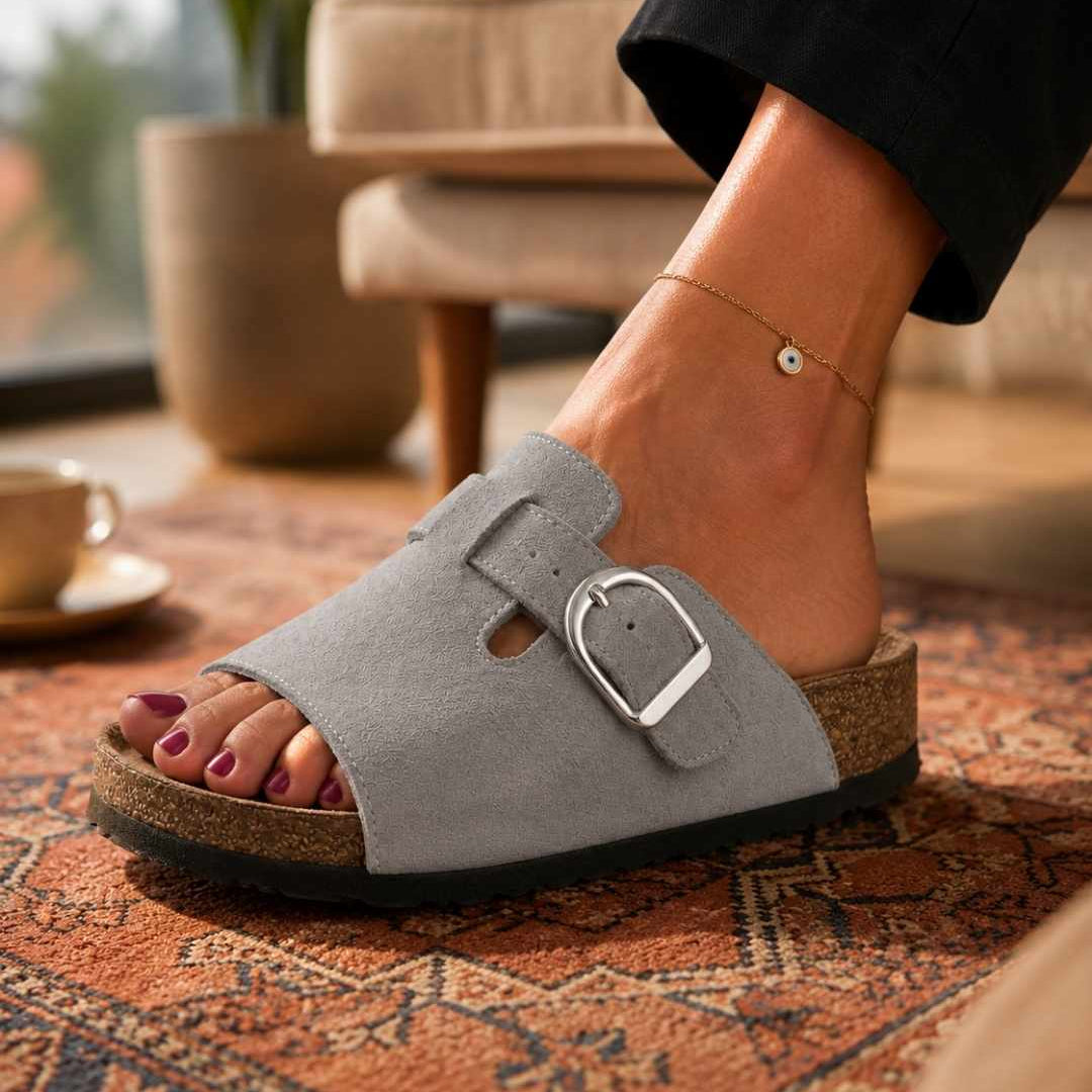 Gray sandal with a buckle worn indoors on a patterned rug.