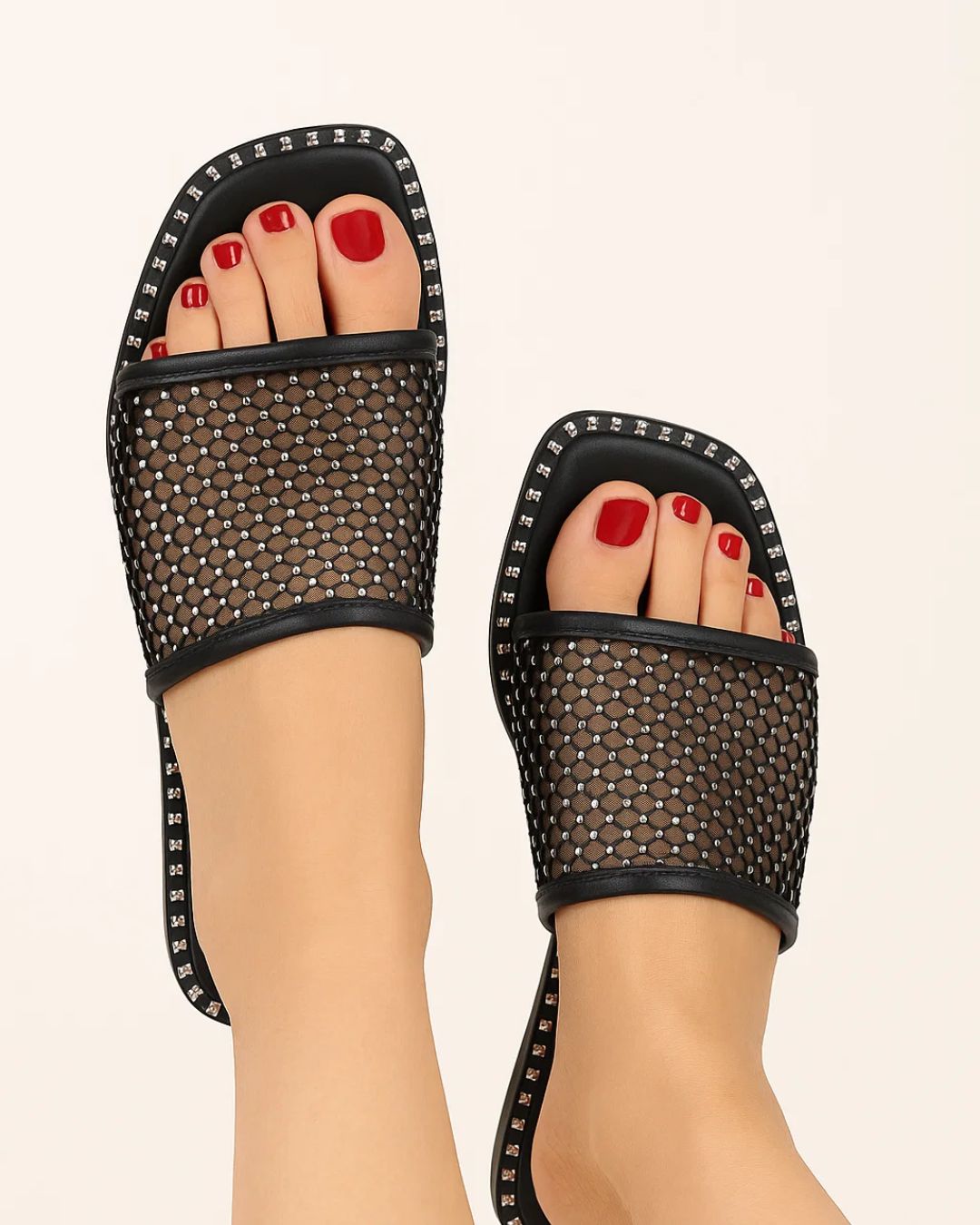Black mesh sandals with studded details worn by a person on a beige background