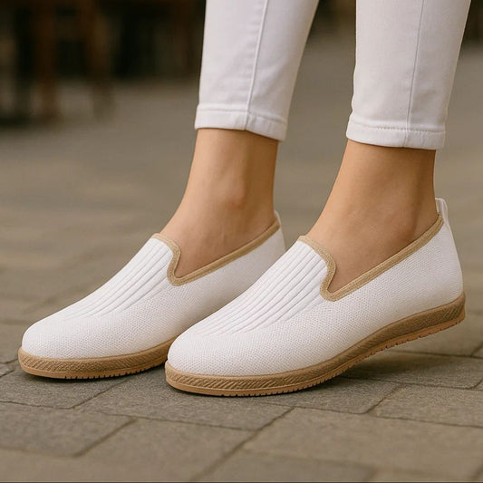 White slip-on shoes with brown soles worn with white pants on a blurred background