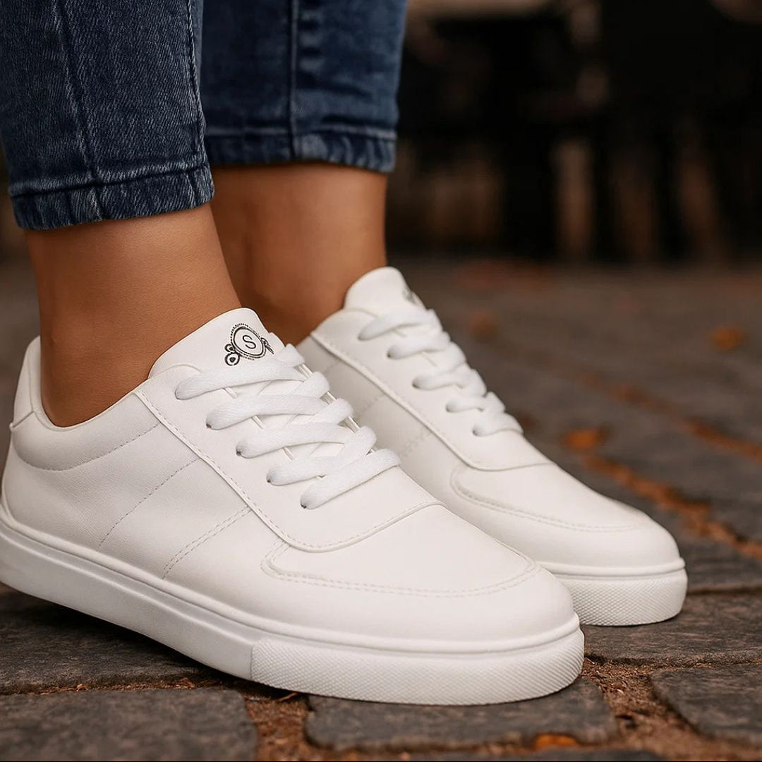White sneakers worn with blue jeans on a stone pavement.