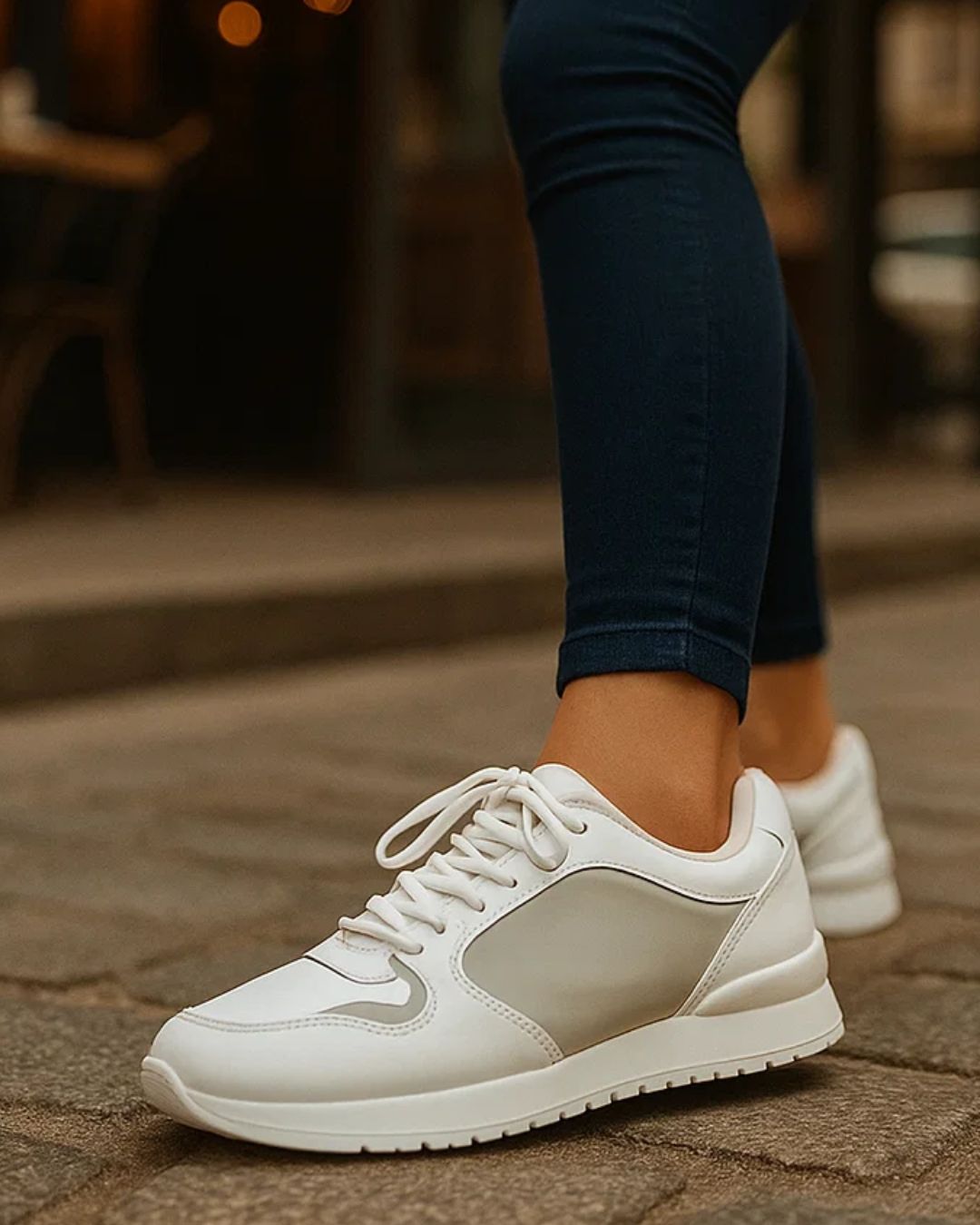 White sneakers worn on a stone pavement with a blurred background