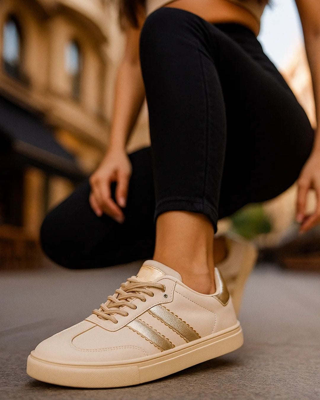 Beige sneakers with gold accents worn by a person sitting on a bench.