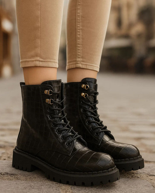 Black lace-up boots worn with beige pants on a blurred background