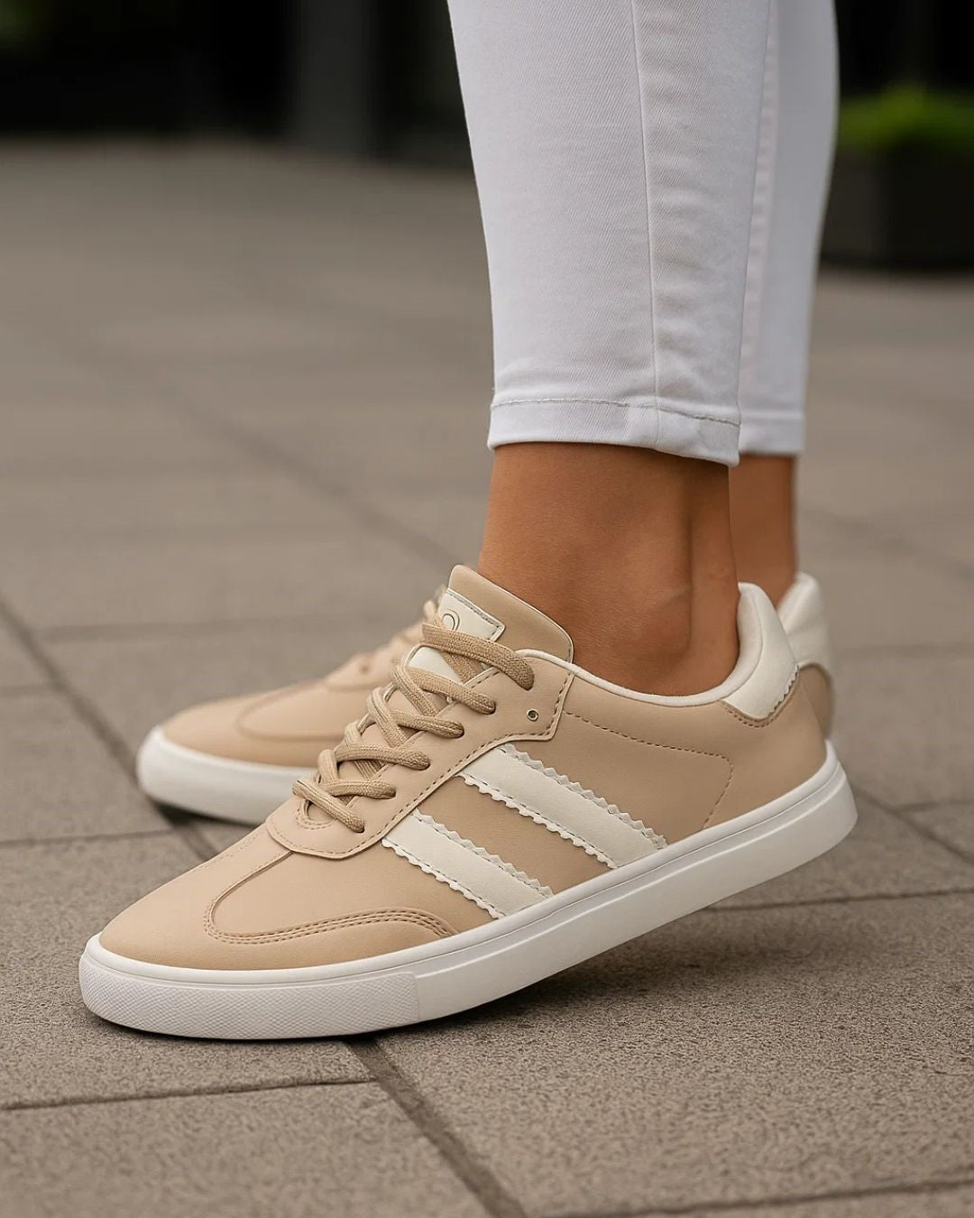 Beige sneakers with white stripes worn on a paved surface