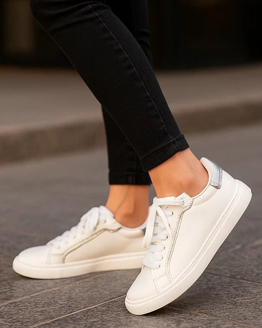 White sneakers worn with black pants on a pavement background
