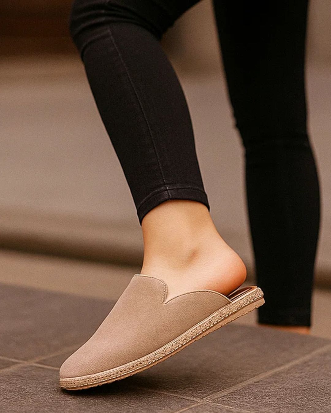 Beige slip-on shoe worn with black pants on a tiled floor.