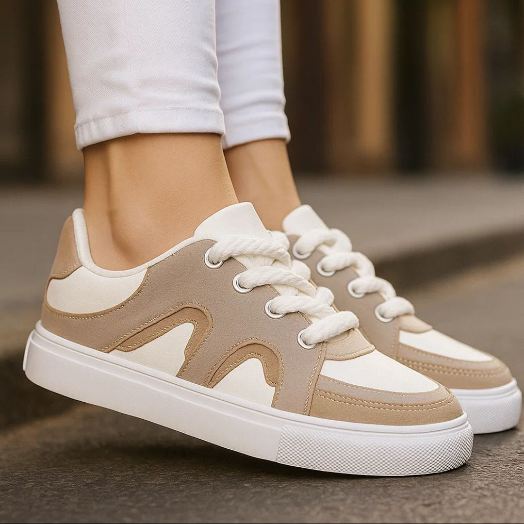 Beige and white sneakers worn with light gray pants on a blurred street background