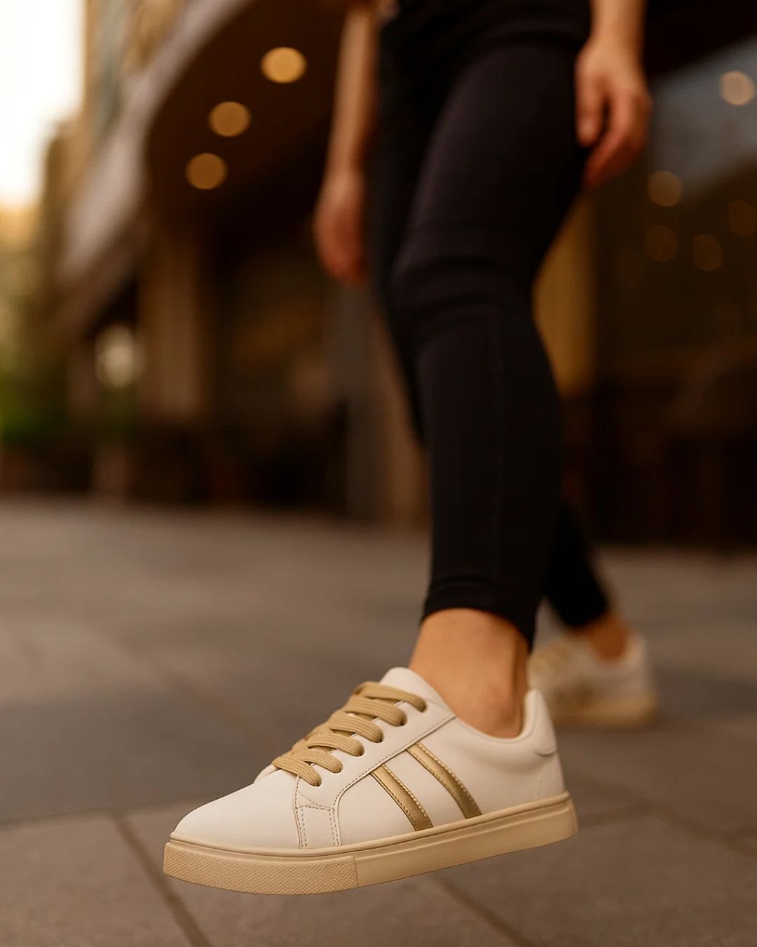White sneakers with gold accents worn by a person on a blurred street background