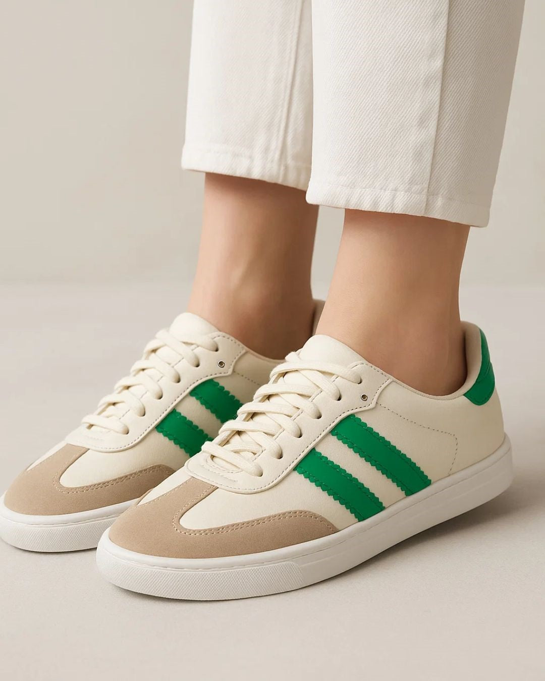Beige sneakers with green stripes worn with white pants on a neutral background