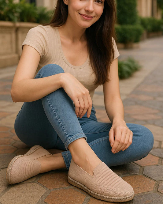 Woman sitting on a stone path wearing beige shoes and blue jeans.