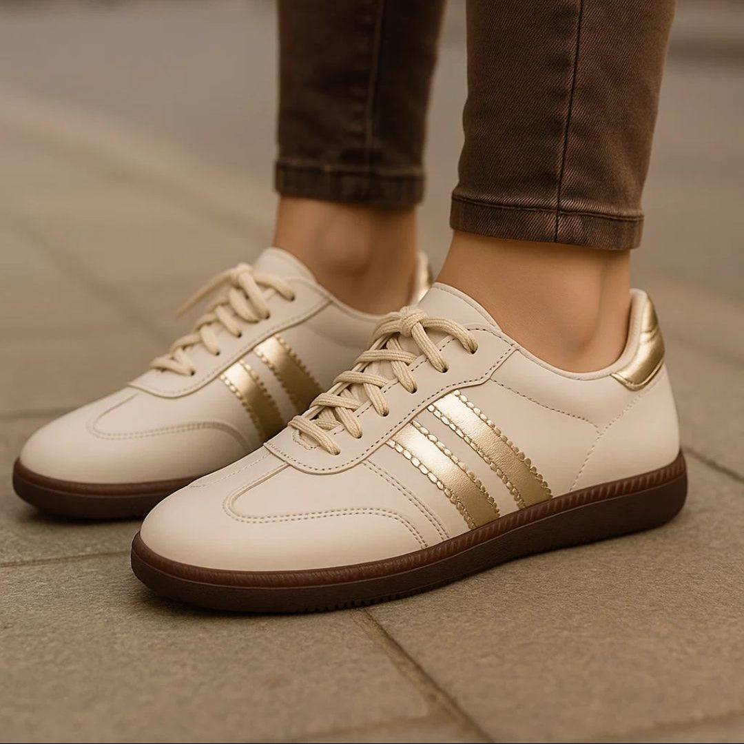 White sneakers with gold accents worn by a person on a pavement.