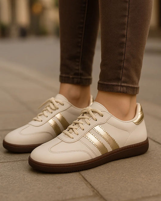 White sneakers with gold accents worn by a person on a pavement.