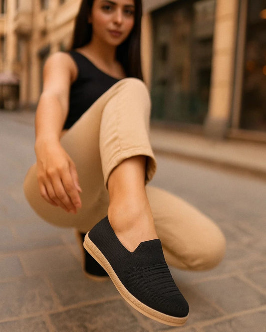 Woman wearing black slip-on shoes with beige pants on a street.