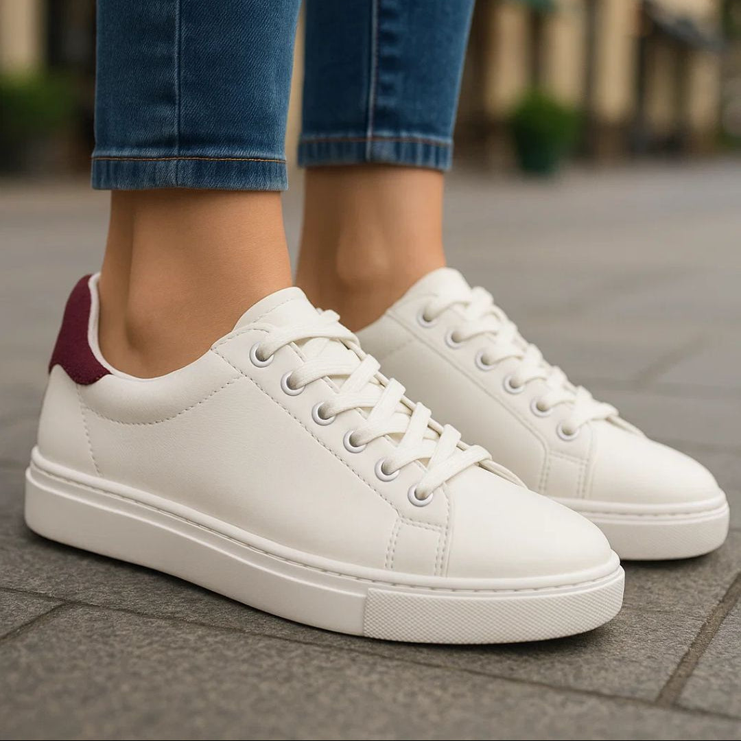 White sneakers with a maroon heel tab worn with blue jeans on a blurred street background