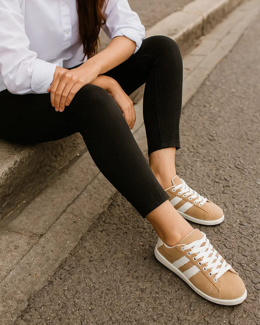 Person wearing beige sneakers with white stripes sitting on a curb.