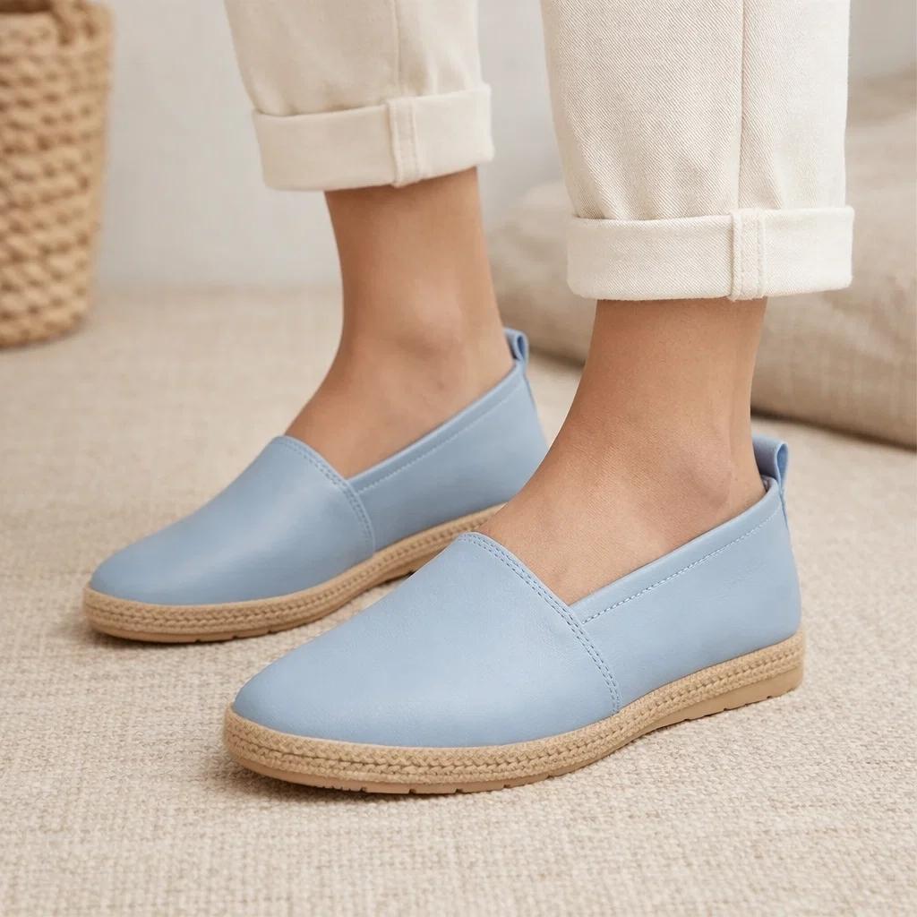 Light blue slip-on shoes with brown soles worn by a person on a beige carpet.