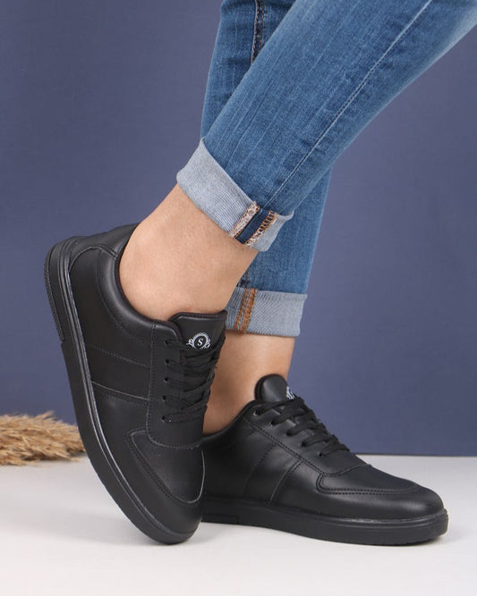 Black sneakers worn with rolled-up blue jeans on a white surface.