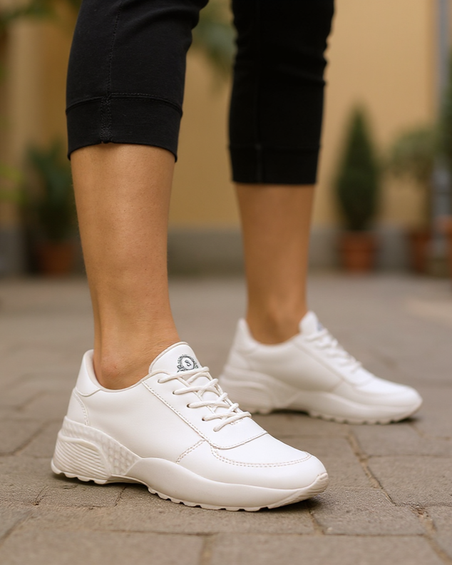 White sneakers worn on a paved surface with a blurred background