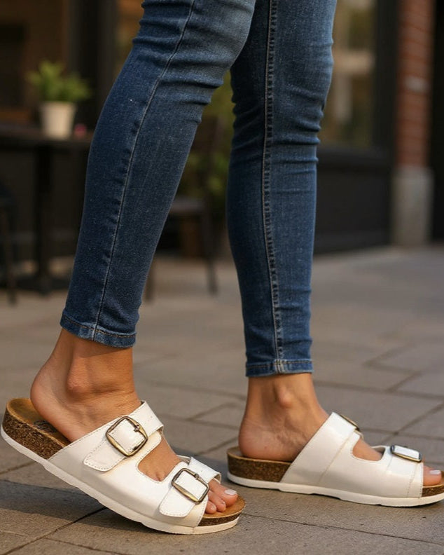 White sandals with brown soles worn with blue jeans on a blurred outdoor background